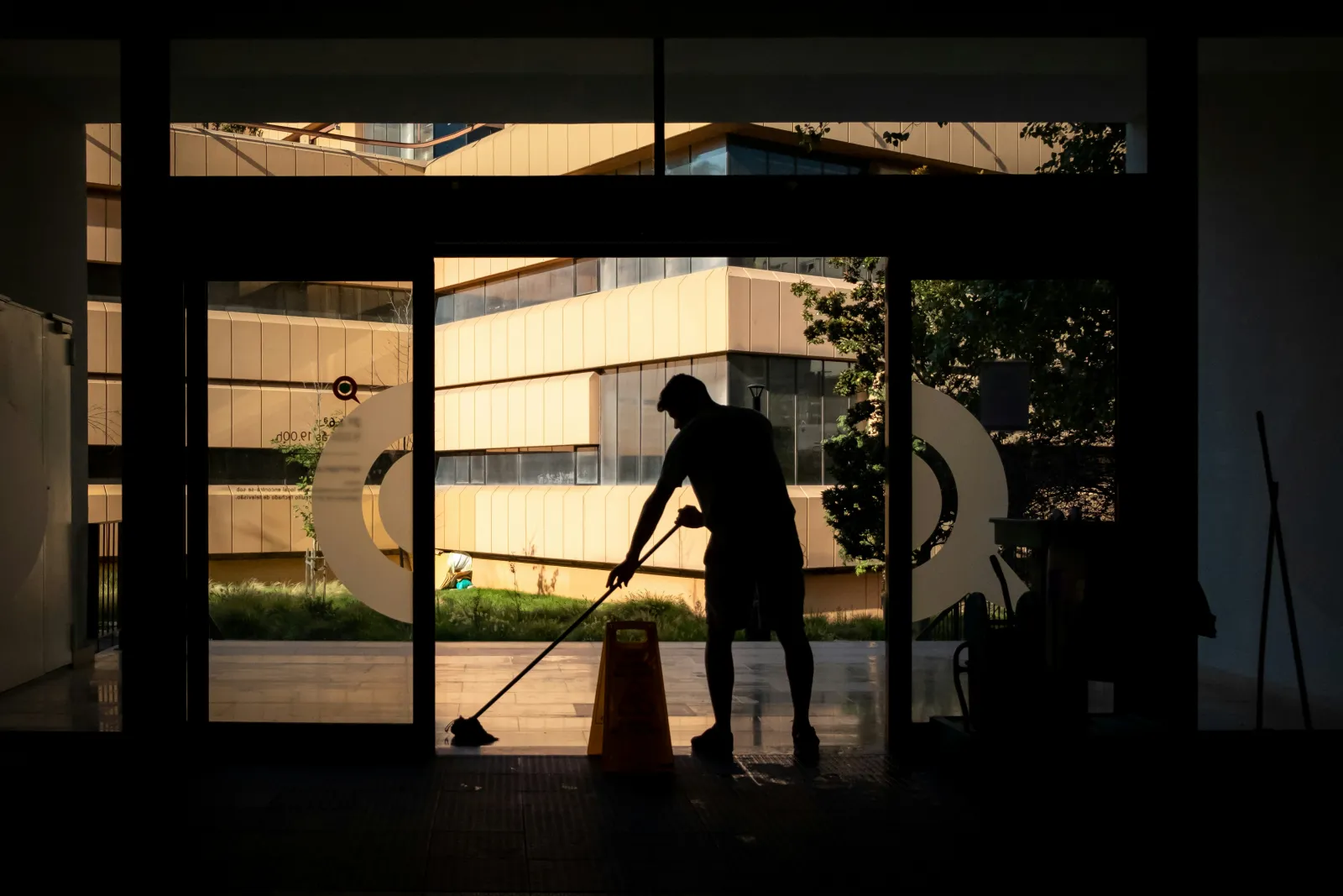 Silhouette einer Reinigungskraft beim Wischen eines Eingangsbereichs