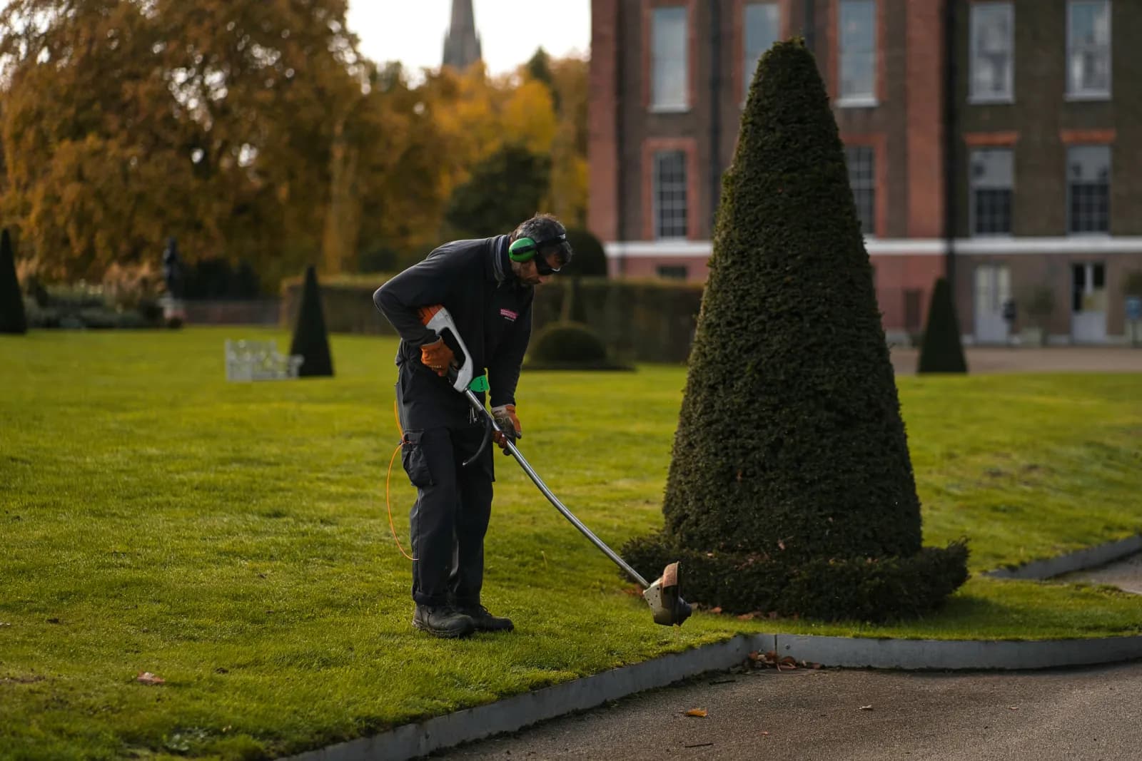 Formschnitt einer Hecke mit einem Motortrimmer in einer Parkanlage